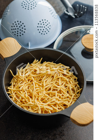 Uncooked spaetzle pasta in pot on kitchen table. Uncooked spaetzle pasta in pot on kitchen table. 113568838