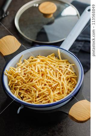 Uncooked spaetzle pasta in colander on kitchen table. 113568849