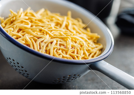 Uncooked spaetzle pasta in colander on kitchen table. Uncooked spaetzle pasta in colander on kitchen table. 113568850