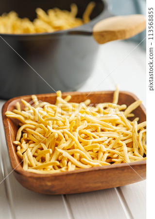 Uncooked spaetzle pasta in bowl on kitchen table. 113568855