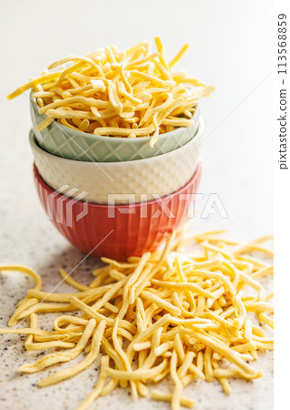 Uncooked spaetzle pasta in bowl on kitchen table. Uncooked spaetzle pasta in bowl on kitchen table. 113568859