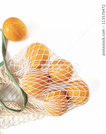 Fresh unpeeled oranges placed in reusable white mesh bag 113570472