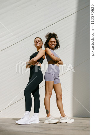 Two young female sportswomen have a rest after morning jogging standing outdoors and looks camera 113570629
