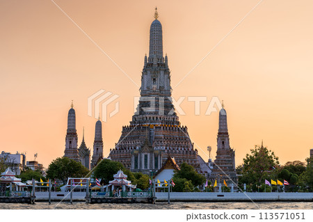 Wat Arun stupa, a significant landmark of Bangkok, Thailand, stands prominently along the Chao Phraya River, with a beautiful sunset sky. 113571051