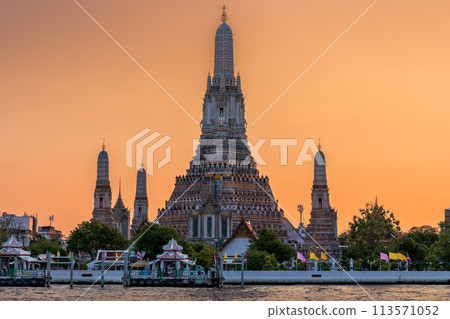 Wat Arun stupa, a significant landmark of Bangkok, Thailand, stands prominently along the Chao Phraya River, with a beautiful sunset sky. 113571052