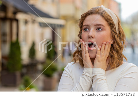 Redhead woman looking surprised at camera shocked by sudden win good victory news wow in city street Redhead woman looking surprised at camera shocked by sudden win good victory news wow in city street 113571758