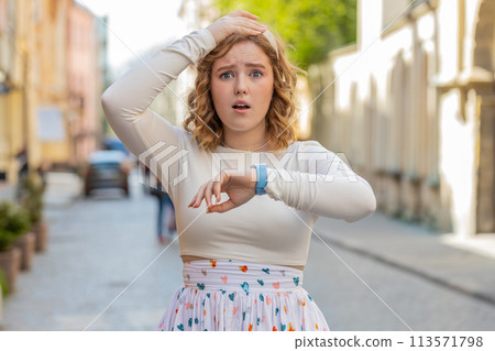 Redhead woman worrying to be punctual with anxiety checking time on watch running late to work 113571798
