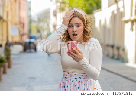 Happy redhead girl use smartphone celebrating win good message news lottery jackpot victory outdoors 113571812