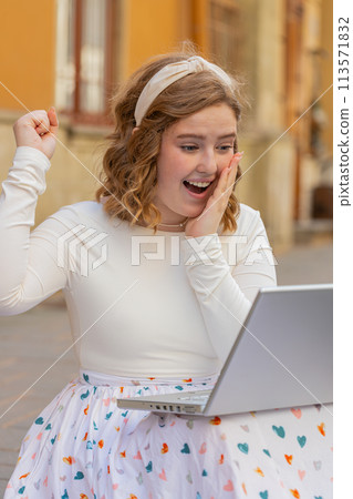 Caucasian happy woman working on laptop celebrate success win money sitting on urban street in city Caucasian happy woman working on laptop celebrate success win money sitting on urban street in city 113571832
