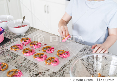 Freshly dipped and still glistening, these crunchy pretzels are lovingly adorned with pink chocolate and a scattering of colorful sprinkles, promising a feast for the senses. 113574606