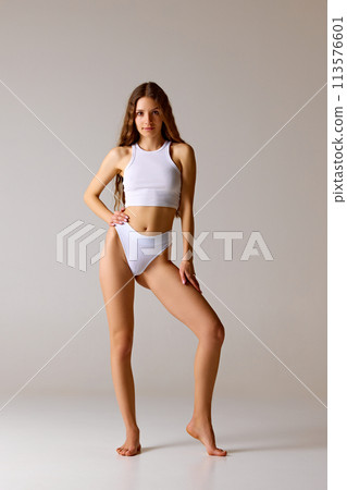 Young beautiful woman posing in lingerie holding hand on hip against white studio background. Model with perfect slim body 113576601