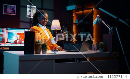 Young woman waving at phone videocall with tutor and classmates, asking for guidance in creating presentations and slideshows. African american student attending online class conference. Camera B. 113577144