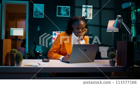 Student working under pressure to finish homework at midnight, trying to respect deadline. Girl rubbing eyes and solving tasks while feeling exhausted, dealing with burnout syndrome. Camera B. 113577166