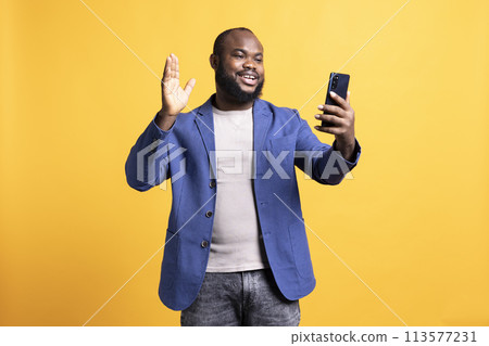 Smiling man having friendly conversation with friends during teleconference meeting using smartphone, studio background. BIPOC person having fun catching up with mates during online videocall Smiling man having friendly conversation with friends during teleconference meeting using smartphone, studio background. BIPOC person having fun catching up with mates during online videocall 113577231