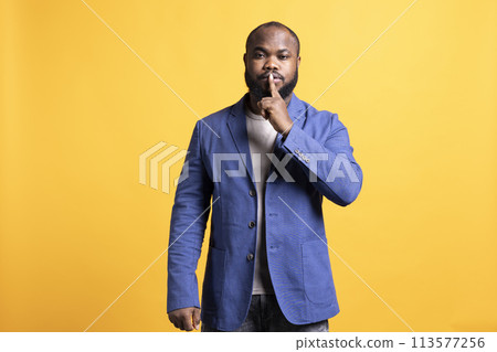 Annoyed african american man doing shushing hand gesturing, irritated by noise, having negative mood. Person placing finger on lips, doing quiet sign gesture, studio background Annoyed african american man doing shushing hand gesturing, irritated by noise, having negative mood. Person placing finger on lips, doing quiet sign gesture, studio background 113577256
