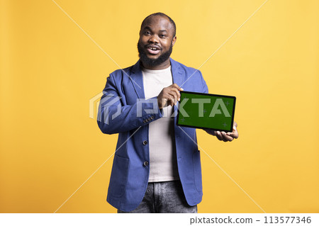 Jolly african american man presenting video on green screen tablet in landscape mode, studio background. Upbeat BIPOC person holding blank copy space chroma key device used for showcasing ads 113577346