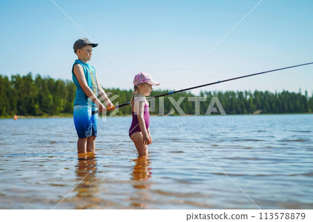 kids fishing standing in the lake. Boy holding a long fish rod 113578879