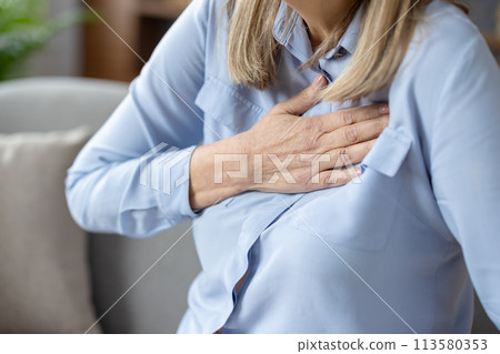 Close-up image of a senior woman experiencing discomfort and holding her chest, possibly indicating heart problems or a heart attack. 113580353