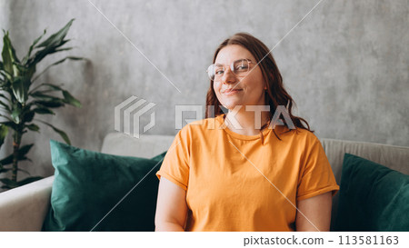 Close up face of young woman in glasses with beautiful smile siting on the sofa couch at home. 30s female rest and spend free spare time in living room indoors. People lounge concept 113581163