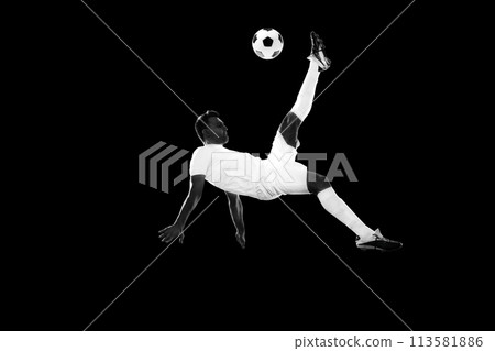 Dynamic image of motivated male soccer playing in motion, training, hitting ball and falling down on lack background. Monochrome Dynamic image of motivated male soccer playing in motion, training, hitting ball and falling down on lack background. Monochrome 113581886