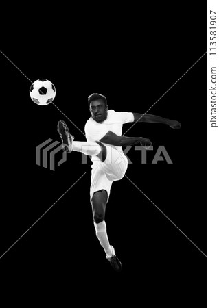 Monochrome dynamic image of young man, soccer player in motion hitting ball in a jump on black background 113581907