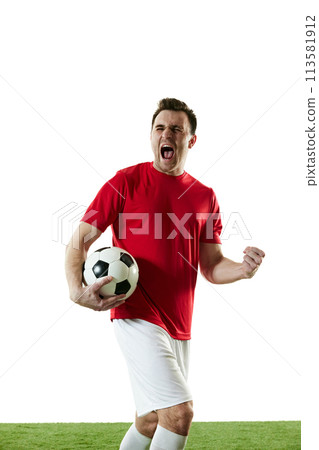 Emotive football player in red t-shirt and white shorts standing with ball on field and shouting isolated on white background 113581912