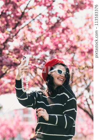 happy woman taking selfie on the phone in front of blooming sakura 113583376