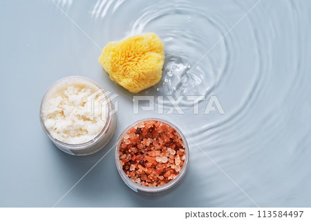 Body scrub, bath salt and natural sponge on a blue background with water. Body scrub, bath salt and natural sponge on a blue background with water. 113584497