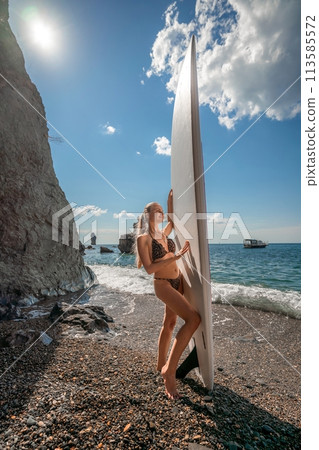 Woman in black bikini sap sea. Portrait of a happy girl on the background of a surfboard in the sea on a sunny summer day 113585572