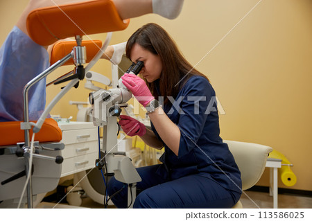 Gynecologist looking in colposcope examining patient on disease 113586025