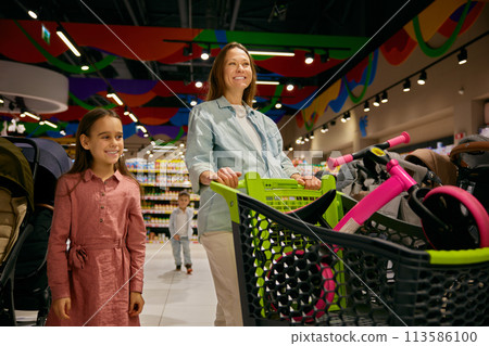 Positive pregnant mother and daughter doing purchases at toys store department 113586100