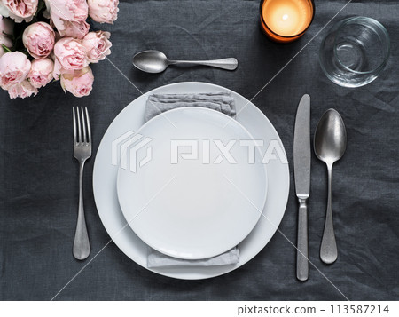 Beautiful table setting on gray linen tablecloth. Festive table setting for wedding dinner with pink spray roses and scented cabdle. Holiday dinner with white plates. Dinner, utensil. Copy space Beautiful table setting on gray linen tablecloth. Festive table setting for wedding dinner with pink spray roses and scented cabdle. Holiday dinner with white plates. Dinner, utensil. Copy space 113587214