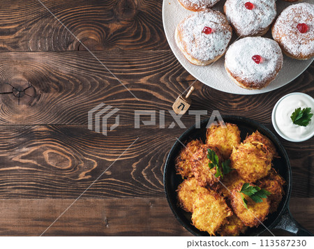 Jewish holiday Hanukkah concept and background. Hanukkah food doughnuts and potatoes pancakes latkes, oil and traditional spinnig dreidl on wooden table. Top view or flat lay. Copy space for text. 113587230