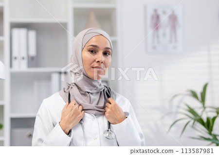 A portrait of a resilient and confident Muslim female doctor wearing hijab in a well-equipped medical office, exuding professionalism and care. A portrait of a resilient and confident Muslim female doctor wearing hijab in a well-equipped medical office, exuding professionalism and care. 113587981