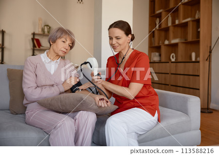 Attentive woman healthcare worker taking blood pressure of senior woman Attentive woman healthcare worker taking blood pressure of senior woman 113588216