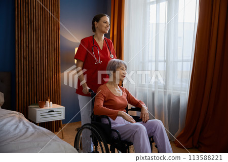 Aged senior woman in wheelchair having professional help at nursing home Aged senior woman in wheelchair having professional help at nursing home 113588221