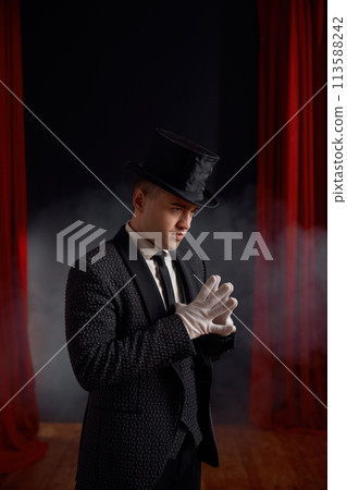 Elegant man magician wearing elegant suit standing in smoke on stage 113588242