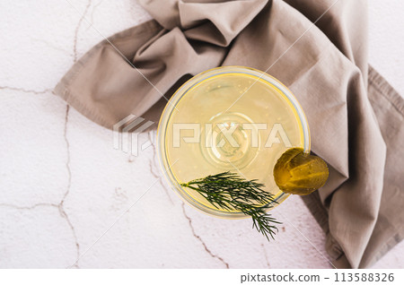Close up of trendy martini cocktail with pickles and dill in a glass on the table top view Close up of trendy martini cocktail with pickles and dill in a glass on the table top view 113588326