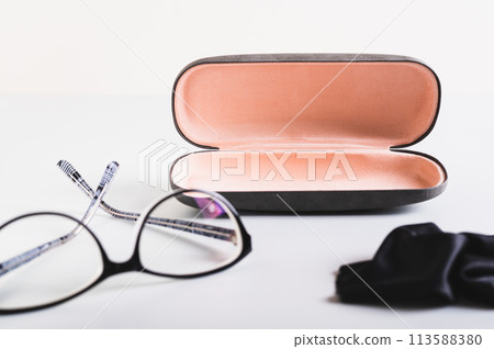 Open hard case for storage, glasses and cleaning cloth nearby on the table 113588380