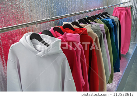 Hoodies on hangers in a clothing store. Row of colorful youth hooded sweatshirt on a clothes rack. 113588612