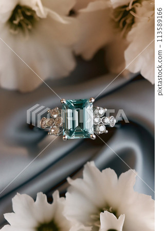 Elegant ring with emerald center stone and diamond accents surrounded by white flowers 113589166