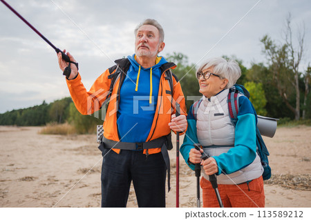 Hiking tourism adventure. Senior couple man woman enjoying outdoor recreation hiking on beach. Happy old people backpackers hikers enjoy walking hike trekking tourism active vacation beauty of nature Hiking tourism adventure. Senior couple man woman enjoying outdoor recreation hiking on beach. Happy old people backpackers hikers enjoy walking hike trekking tourism active vacation beauty of nature 113589212