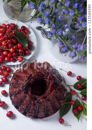 Chocolate cake with sweet cherry, vintage kettle and bouquet of blue flowers on white background.. Chocolate cake with sweet cherry, vintage kettle and bouquet of blue flowers on white background.. 113589395