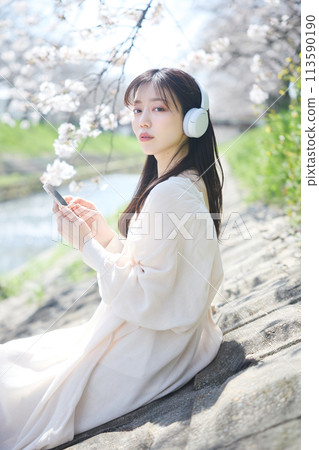 A woman listening to music under the cherry blossoms 113590190