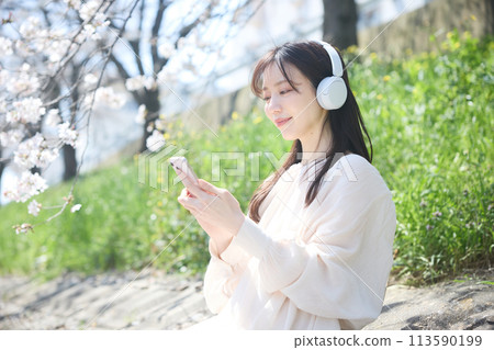 A woman listening to music under the cherry blossoms 113590199