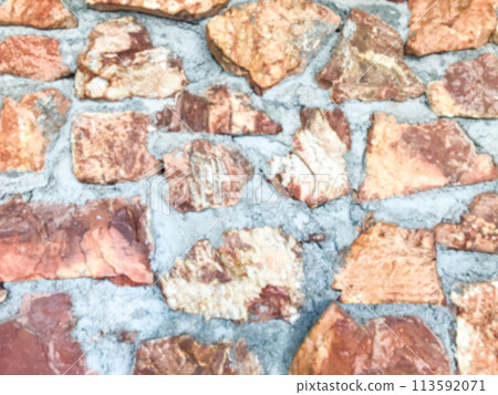 Close up and blurring of the old patterned stone wall and has cement to keep it strong. The rocks are stacked. The stones are brown, orange, gray, beautiful. Background landscape. 113592071