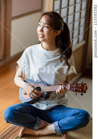 A woman practicing the ukulele on the veranda 113593392