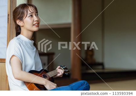 A woman practicing the ukulele on the veranda 113593394