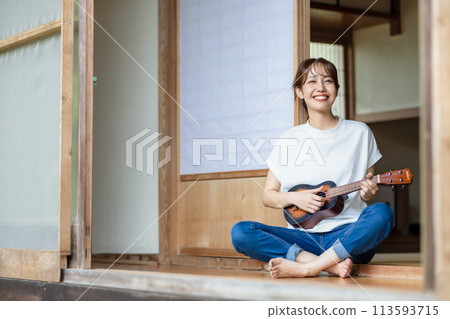 A woman practicing the ukulele on the veranda 113593715