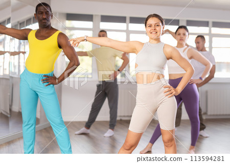 Expressive young woman learning modern street dancing during multinational group class in choreographic studio Expressive young woman learning modern street dancing during multinational group class in choreographic studio 113594281